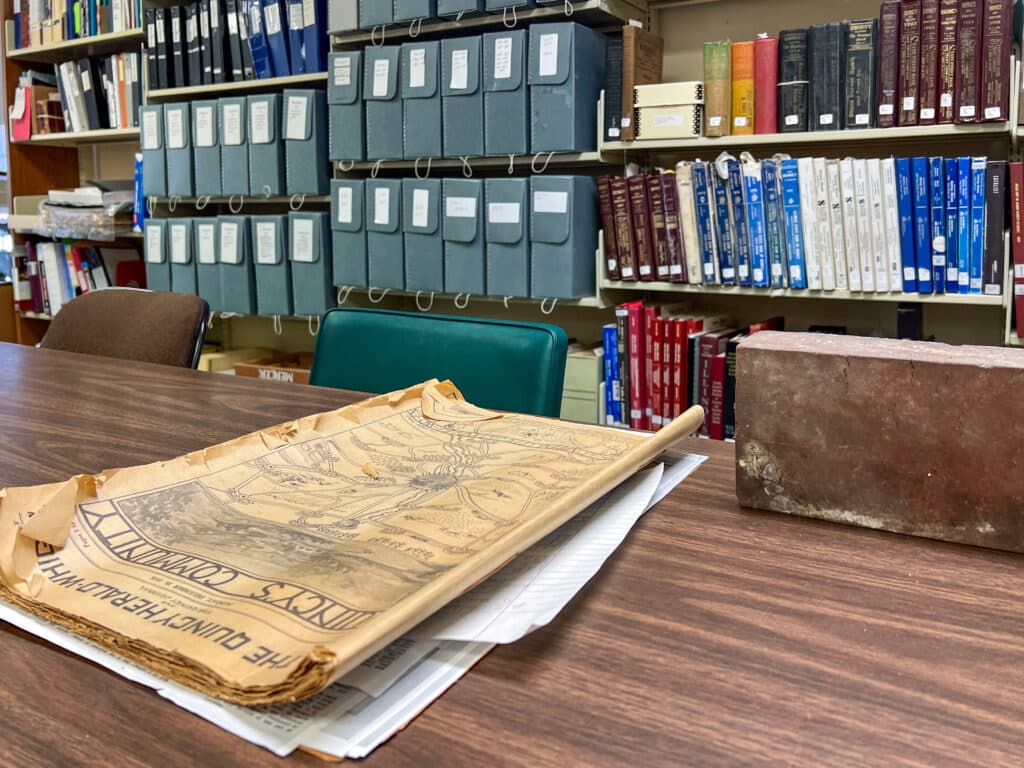 A yellowed document sitting on a wooden table with bookshelves in the background