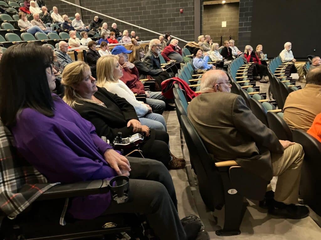A group of people sitting in an audience watching a lecture