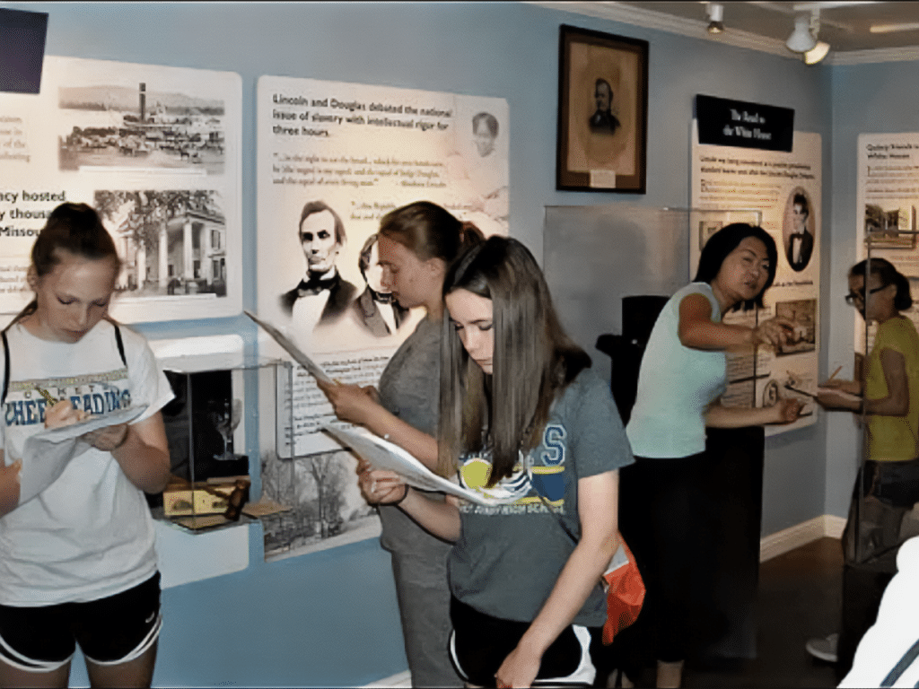 Girls with papers walking in an exhibit with a teacher in the background